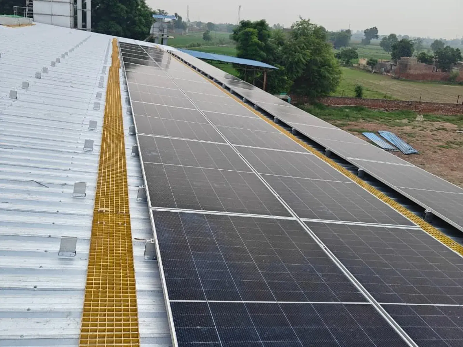 Avaada TOPCon modules beside a yellow FRP walkway on the tin-shed roof