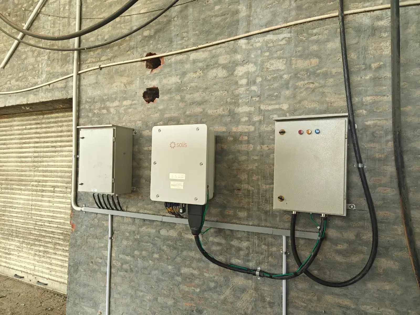 Solis inverter mounted between distribution boxes on a brick wall