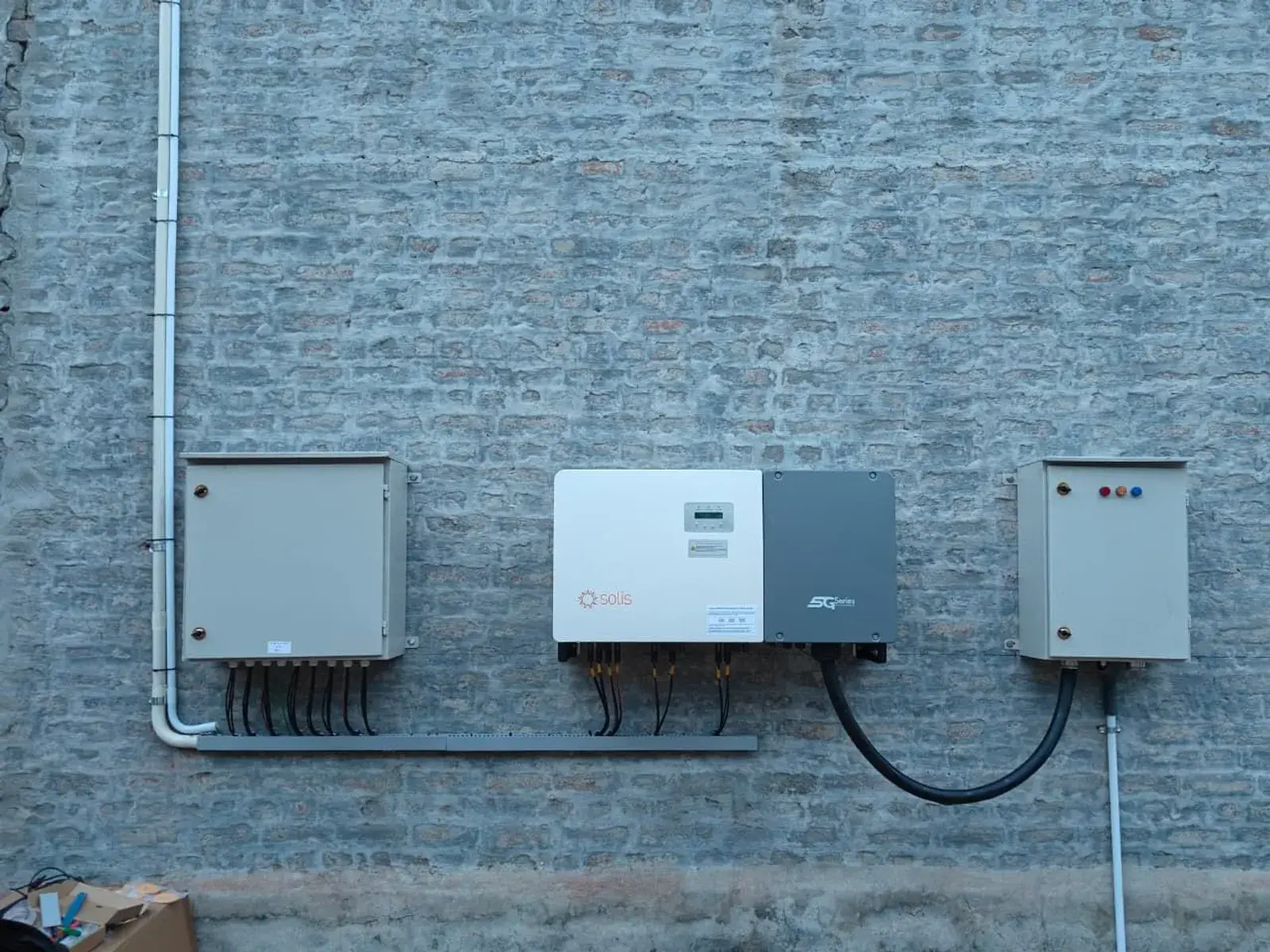 Solis three-phase inverter mounted between distribution boxes on a brick wall