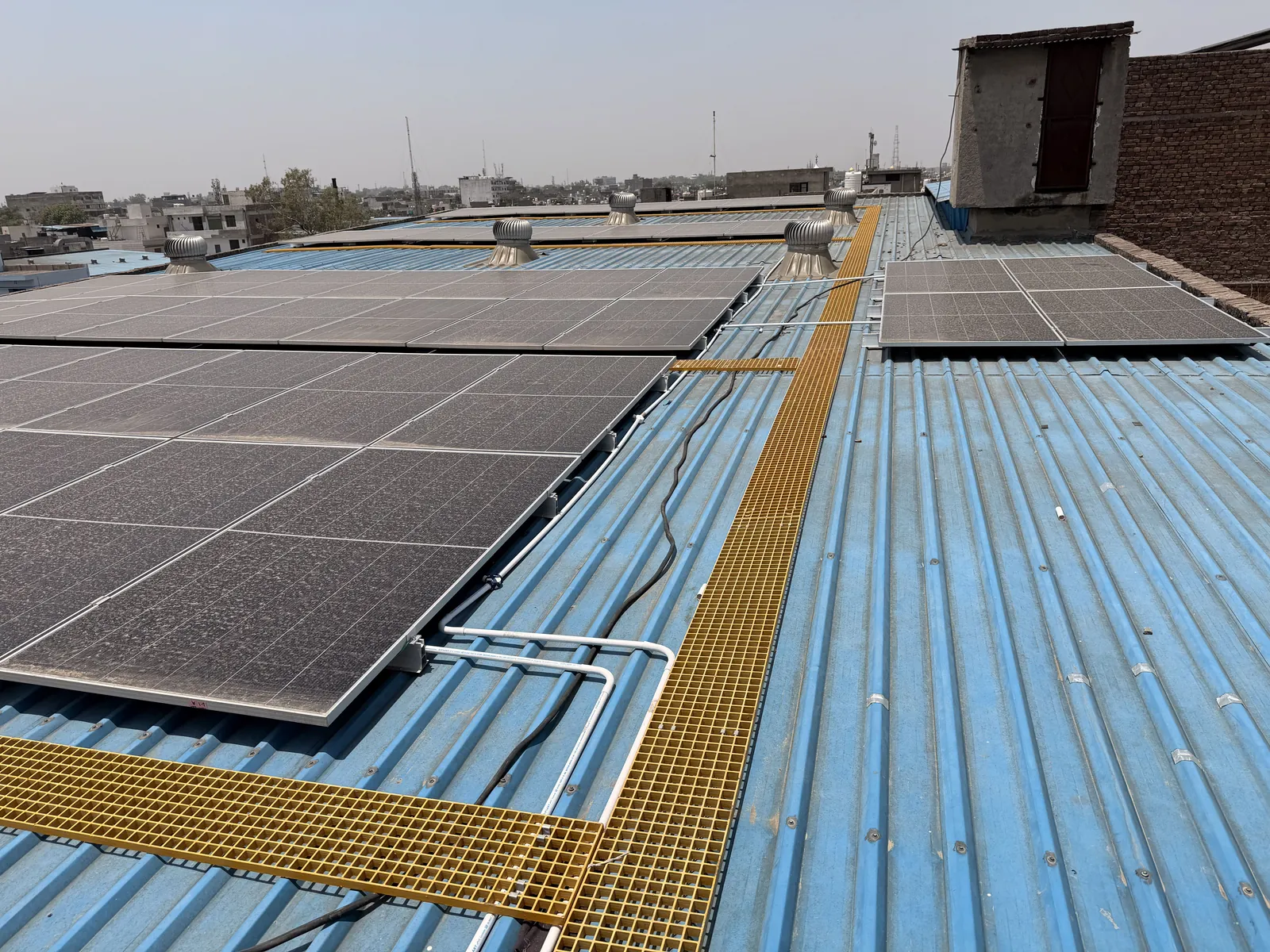 Solar array beside a yellow FRP walkway on the Jagan Hosiery tin-shed roof